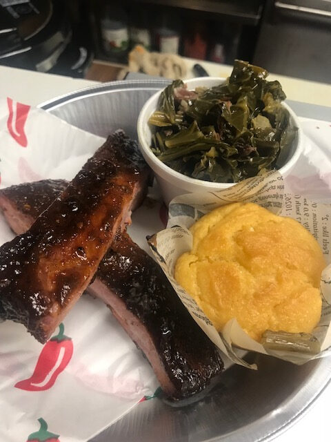 A plate of food with ribs, greens and mashed potatoes.